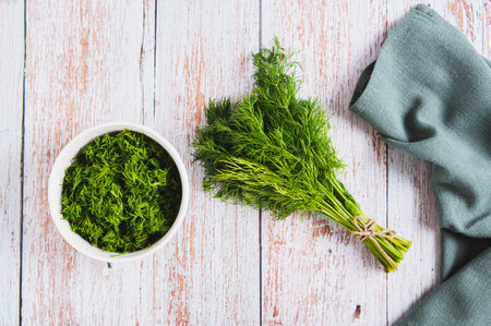 Bunch of fresh dill and chopped dill in a bowl on a table top viewの写真素材