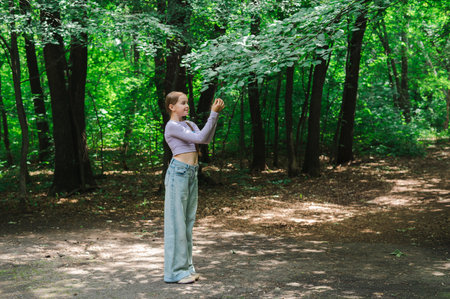 Teenage girl looking at leaves on tree branch in parkの写真素材
