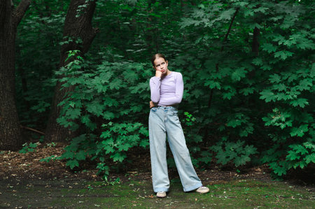 Thoughtful teenage girl standing in the forest during the dayの写真素材
