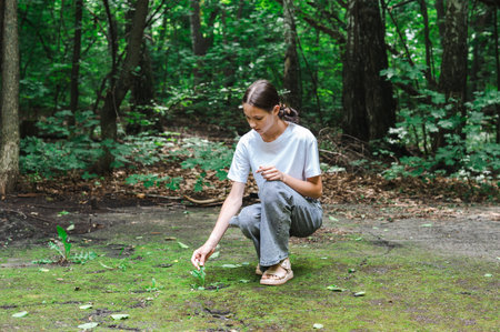 Teenage girl touches a sprout that has emerged from a path in a parkの写真素材