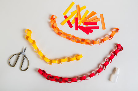 Multicolored handmade paper chains, scissors, glue and paper strips top viewの写真素材