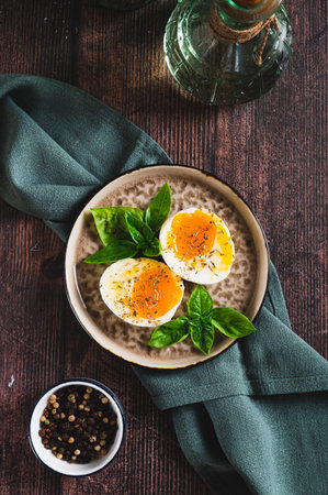 Spicy soft-boiled egg halves and basil on a plate on a table top and vertical view