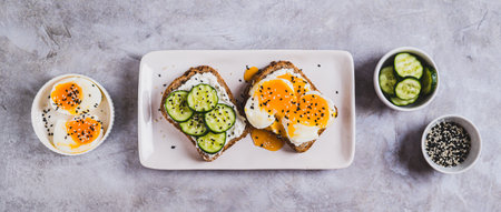 Cucumber slices and soft-boiled eggs on ricotta bread with nesame on a plate top view web bannerの写真素材