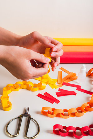 A girl's hands fold a strip of paper to make a paper chain vertical viewの写真素材