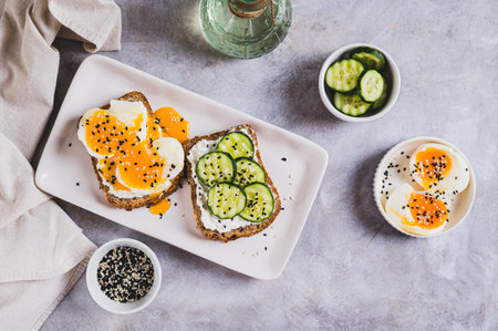Open sandwiches with ricotta, cucumber and soft-boiled egg on a plate on a table top viewの写真素材