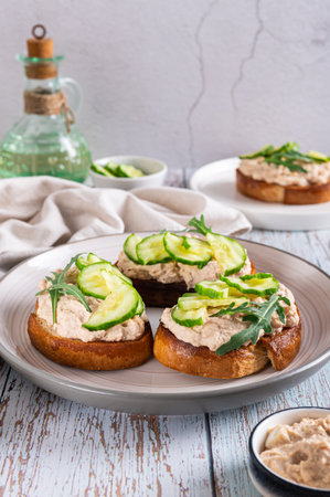Appetizing sandwiches with code liver pate, cucumber and arugula on a plate vertical viewの写真素材