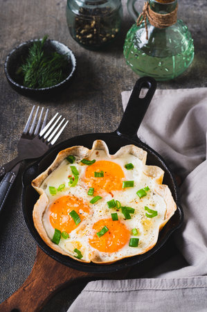 Fried eggs with green onions in a tortilla on a frying pan on the table vertical viewの写真素材
