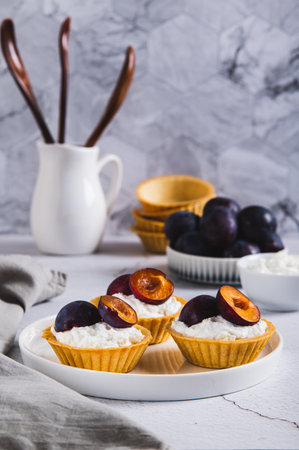 Mini tartlets with cottage cheese and plum on a plate on the table vertical viewの写真素材