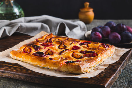 Sweet focaccia with plum on a wooden board on the tableの写真素材