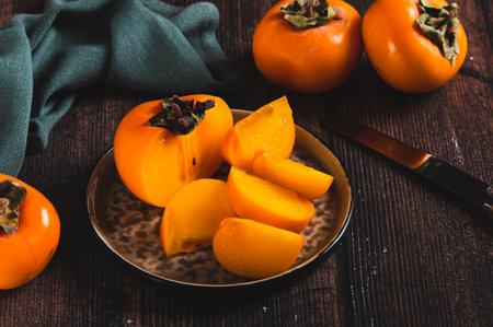 Pieces and halves of persimmon fruit on a plate and on a tableの写真素材