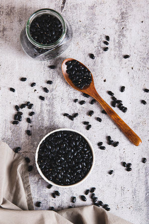 Fresh black beans in a bowl and in a jar on the table top and vertical viewの写真素材