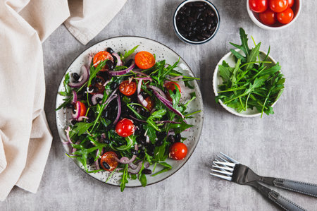 Fresh salad with black beans, cherry tomatoes, arugula and red onion on a plate top viewの写真素材
