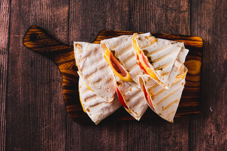 Close up of sandwiches with sausage, cheese and tomatoes in a tortilla on a board top viewの写真素材