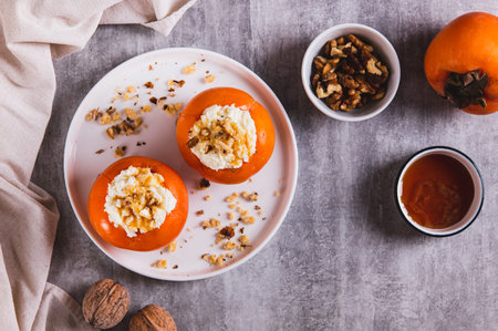 Ripe persimmon filled with cottage cheese, honey and nuts on a plate on the table top viewの写真素材
