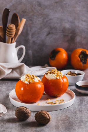 Ripe persimmon filled with cottage cheese, honey and nuts on a plate on the table vertical viewの写真素材