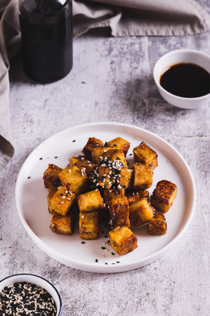 Roasted tofu cubes in garlic soy sauce with sesame seeds on a plate on the table vertical viewの写真素材