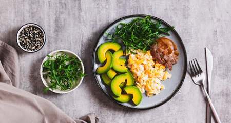 Fried eggs and bacon, fresh avocado and arugula on a plate on the table top view web banner