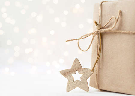 Wooden Christmas toy star and gift in craft paper on light background with bokeh and copy spaceの写真素材