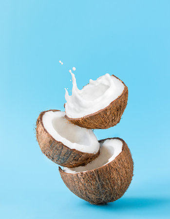 Cracked coconut with splashes of milk on blue background.の写真素材