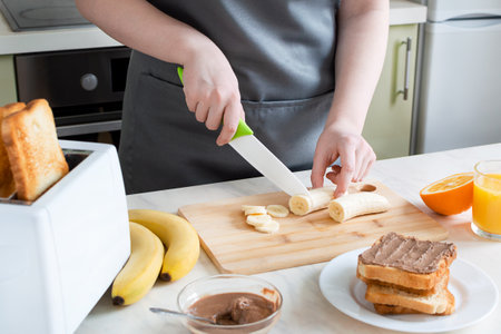 Woman cuts banana for toast for breakfast. European breakfast with toast, banana and juiceの写真素材