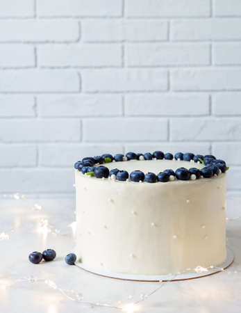 White cake with a wreath made of blueberries and mint on table with garland.の写真素材