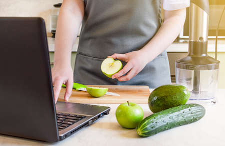 housewife uses laptop and prepares fresh fruis and vegetables for smoothies.