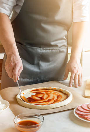 chef smears tomato sauce on the pizza doughの写真素材