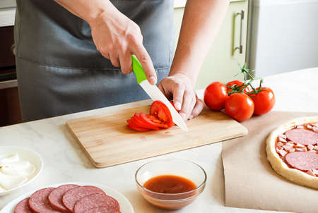 hands chefs cut tomatoes, cooking pizza ingredients on wooden boardの写真素材