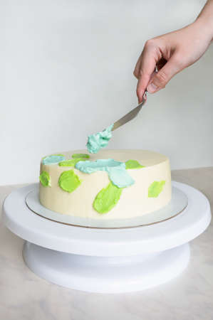 hands with a spatula decorate the cake with green and blue cream.