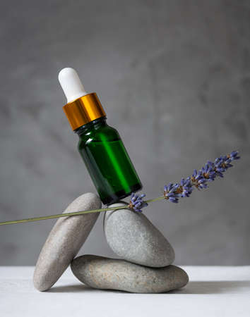 green glass bottle and lavender branch balancing on stones.