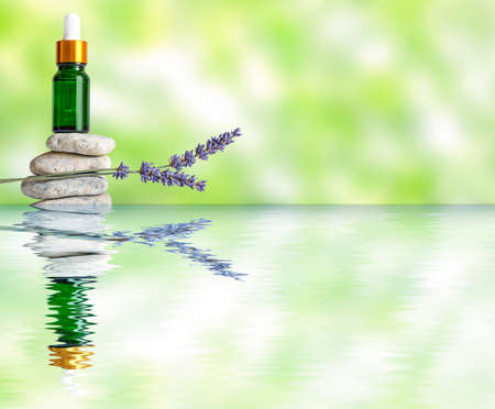 green glass bottle on stones and sprig of lavender on a green blurry background with reflection in water.の写真素材