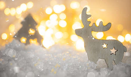 Wooden deer and christmas tree decorations in a snowdrift of snow against the background of golden bokehの写真素材