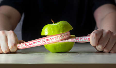 concept of a diet. hands hold the measuring tape around the appleの写真素材