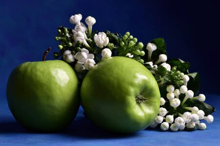 Green apples decorated with white flowers, on a beautiful blue background, in an artistic style, still-life, close-upの写真素材