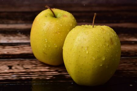 Golden apples, wet, with water drops, on a brown, textured backgroundの写真素材