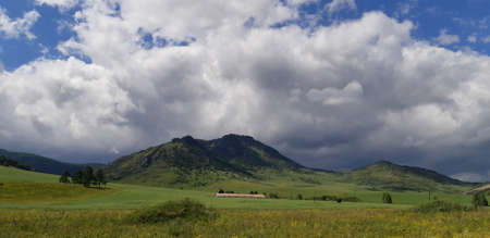 A photograph of a landscape with mountains, trees, grass and clouds. Natural background. High quality photoの写真素材