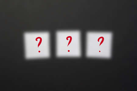 Ready-made inscription with three question marks on white squares of paper on a dark blurred...