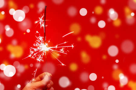 Sparkler, bright holiday sparks fireworks, close-up on a red background. The concept of celebrating Christmas and New year.の写真素材