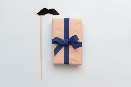 Gift box with kraft paper with a mustache on a light blue background. Flat lay for father's day concept.の写真素材