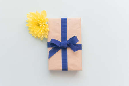 Gift box with kraft paper, a blue ribbon and a yellow flower on a light blue background. Flat lay for father's day concept.の写真素材
