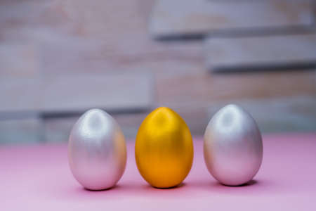Three eggs stand on the surface, silver and gold