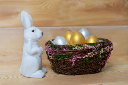 One white toy rabbit on a wooden background next to a basket of eggs