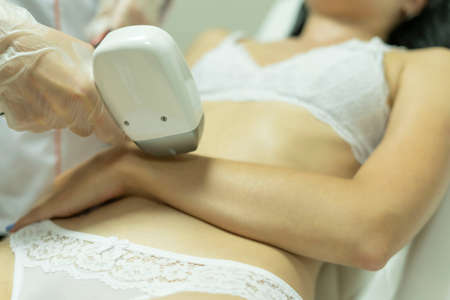 A brunette girl is lying on her back, she is getting laser hair removal on her armの写真素材