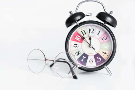 Black alarm clock on a white background. Glasses lie next to the clock