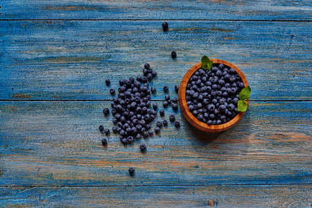 View from above on a wooden table with blue peeling paint, there is a wooden bowl with fresh just picked berriesの写真素材