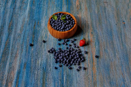 View from above on a wooden table with blue peeling paint, there is a wooden bowl with fresh just picked berries, lies near bright ripe strawberriesの写真素材