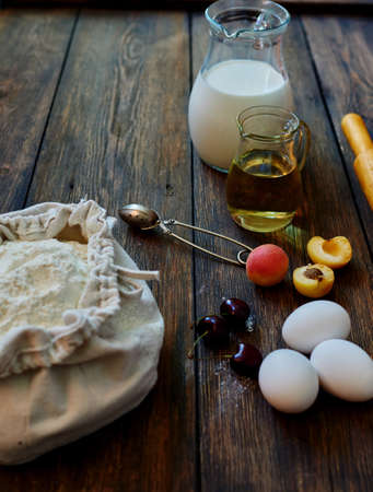 On a wooden table textural worth jug of milk, extra virgin olive oil, cherries, apricots, flaxseed flour bagの写真素材