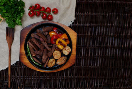 The meat cut into long thin slices, cook laid out in a round cast-iron skillet, along with meat baked peppers and onions until golden brown, cooked tomatoes and greens on saladの写真素材