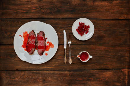 On a dark textural oak table, serving dinner on a white plate on two pieces of beef fried in rapid fire, standing next to the sauceの写真素材