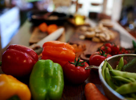 Handful of fresh vegetables on the table, next to the board housewife chopped carrots in alluminum deep cup is pea pods, can be seen in the background olive oil and soy sauce for refuelingの写真素材